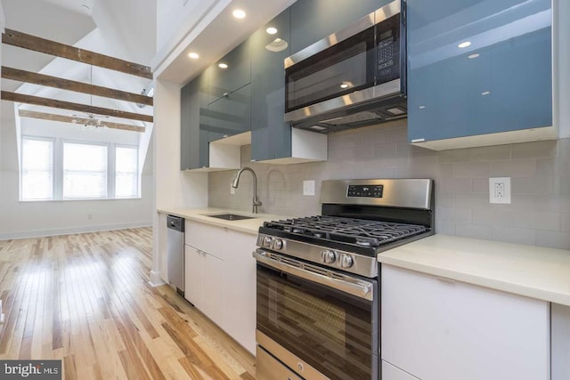 kitchen with beam ceiling, stainless steel appliances, a sink, and light countertops