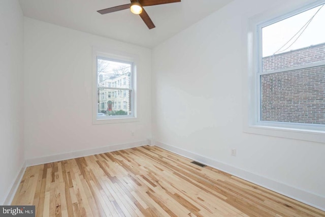 empty room with light wood-style flooring, a ceiling fan, visible vents, and baseboards