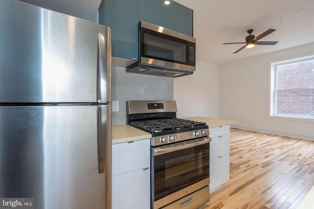 kitchen featuring light countertops, light wood-style flooring, backsplash, appliances with stainless steel finishes, and modern cabinets