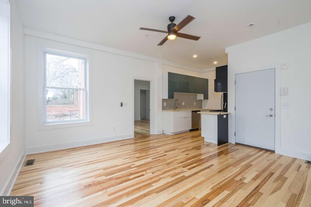 unfurnished living room featuring a sink, a ceiling fan, baseboards, visible vents, and light wood-style floors