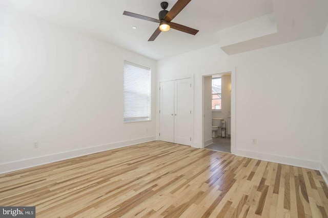 unfurnished bedroom featuring connected bathroom, wood finished floors, a ceiling fan, baseboards, and a closet