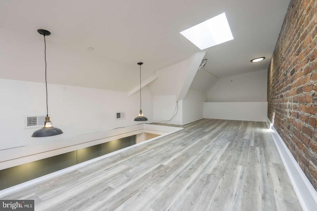 additional living space with brick wall, vaulted ceiling with skylight, wood finished floors, and visible vents