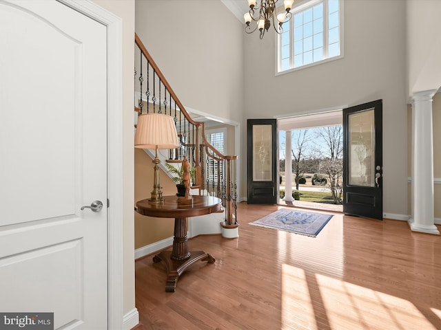 foyer entrance featuring wood finished floors, stairway, baseboards, a chandelier, and ornate columns