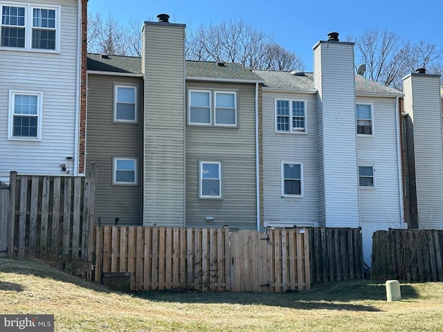 view of side of home with a chimney, fence, and a lawn