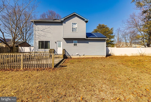 rear view of house with solar panels, a yard, and fence