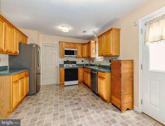 kitchen with stainless steel appliances, a sink, backsplash, brown cabinetry, and dark countertops