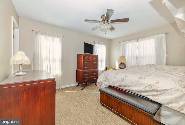 bedroom featuring light carpet, ceiling fan, multiple windows, and baseboards