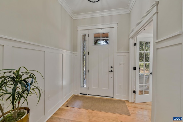 entrance foyer featuring light wood-style floors, ornamental molding, a decorative wall, and wainscoting