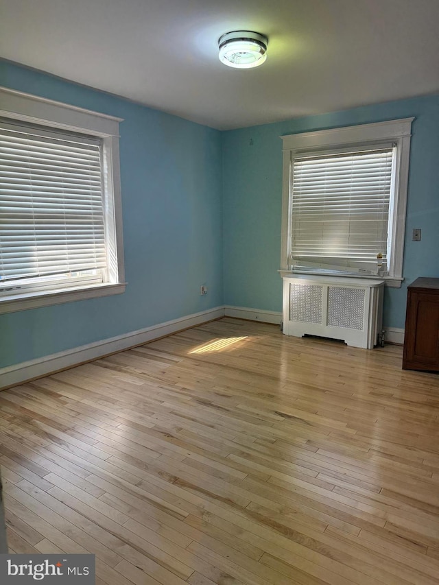 spare room featuring light wood-type flooring, radiator, and baseboards