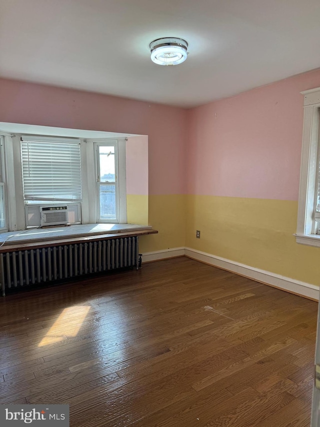 unfurnished room featuring cooling unit, radiator, baseboards, and wood finished floors