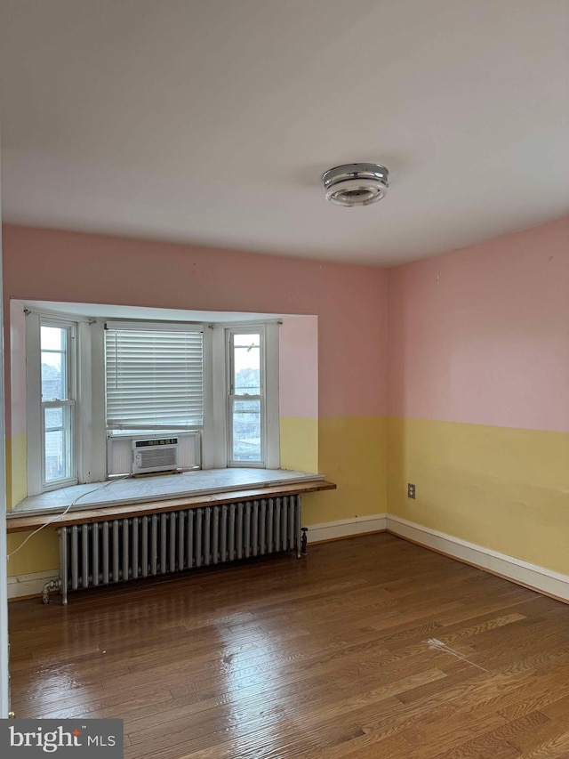 empty room with baseboards, radiator heating unit, cooling unit, and wood finished floors