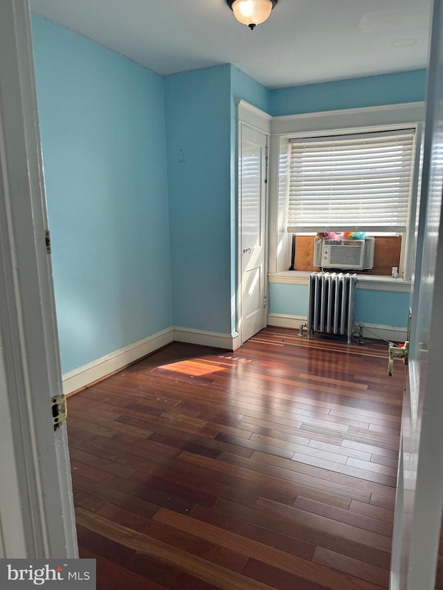 unfurnished room with baseboards, cooling unit, wood finished floors, and radiator