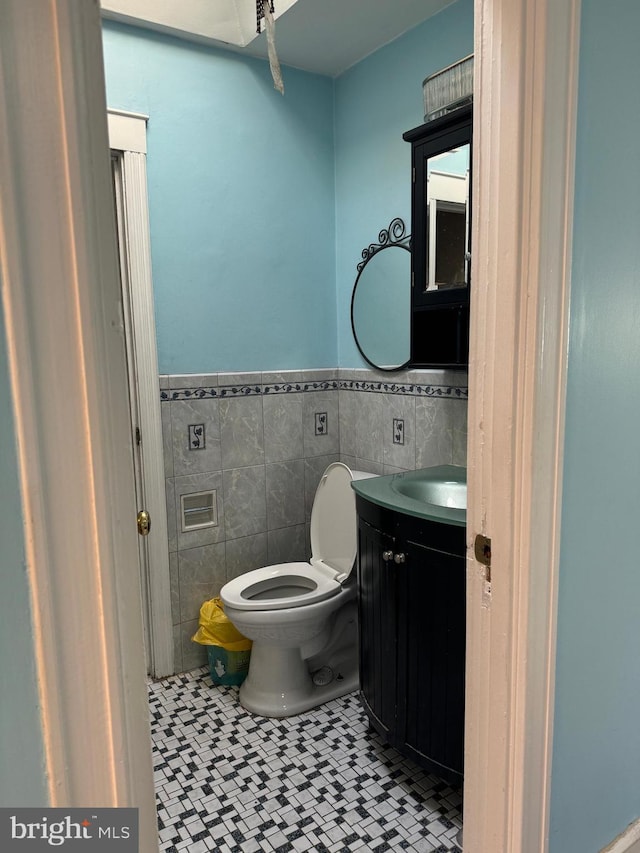 bathroom featuring toilet, a wainscoted wall, tile patterned flooring, vanity, and tile walls