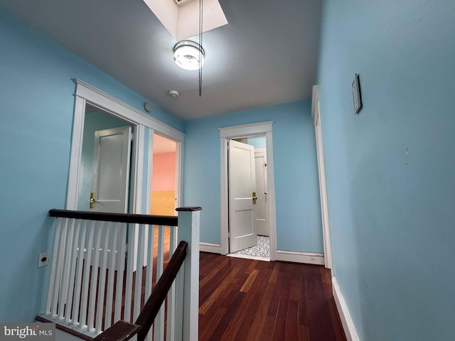 corridor with baseboards, an upstairs landing, and wood finished floors