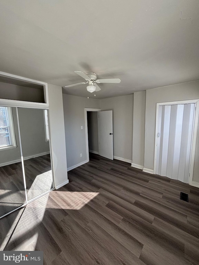 unfurnished bedroom featuring a ceiling fan, visible vents, baseboards, a closet, and dark wood-style floors