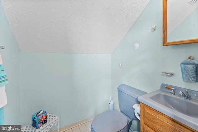 bathroom with a textured ceiling, lofted ceiling, toilet, vanity, and tile patterned floors