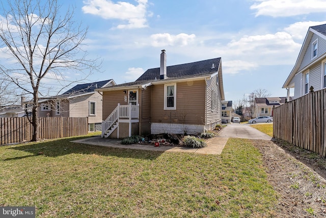 rear view of property featuring a yard, a chimney, and fence