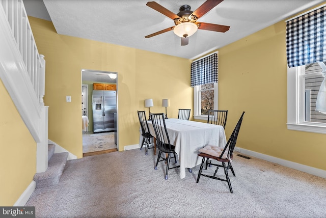 carpeted dining space featuring a ceiling fan, stairway, visible vents, and baseboards