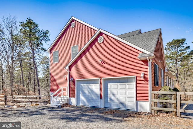 view of side of property featuring roof with shingles, an attached garage, and fence