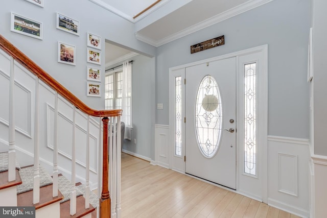 entrance foyer with a wainscoted wall, light wood finished floors, a decorative wall, stairway, and ornamental molding