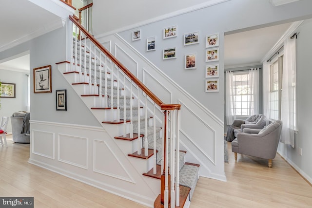 staircase with crown molding, a decorative wall, and wood finished floors