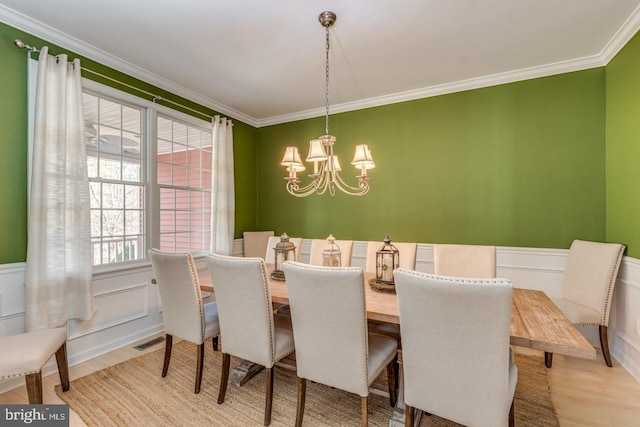 dining space featuring a wainscoted wall, visible vents, light wood-style floors, ornamental molding, and an inviting chandelier