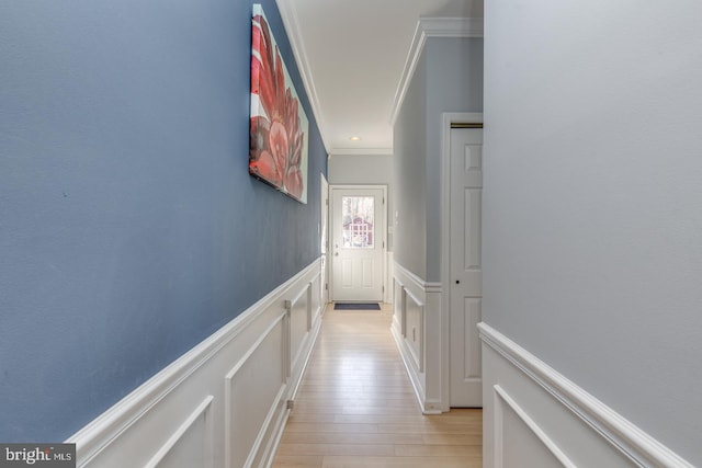 hall featuring light wood-style floors, wainscoting, crown molding, and a decorative wall