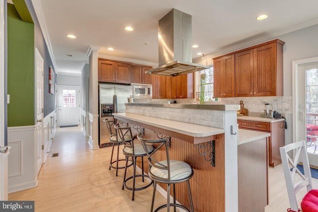 kitchen with island range hood, a kitchen island, appliances with stainless steel finishes, brown cabinets, and crown molding