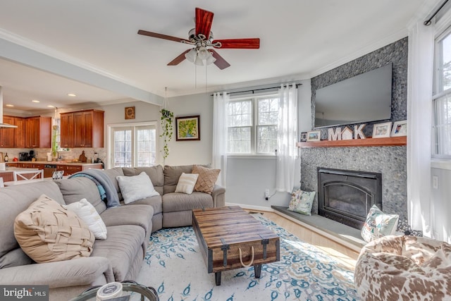 living room with wood finished floors, a ceiling fan, baseboards, a glass covered fireplace, and crown molding