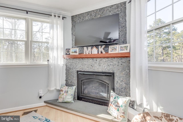 room details with a large fireplace, wood finished floors, visible vents, baseboards, and crown molding