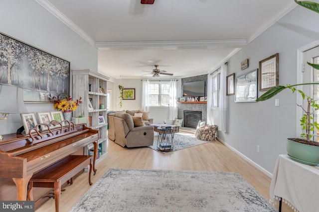 living area featuring a glass covered fireplace, wood finished floors, crown molding, and ceiling fan