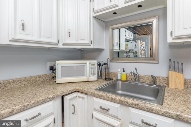 kitchen featuring white cabinets, light countertops, a sink, and white microwave