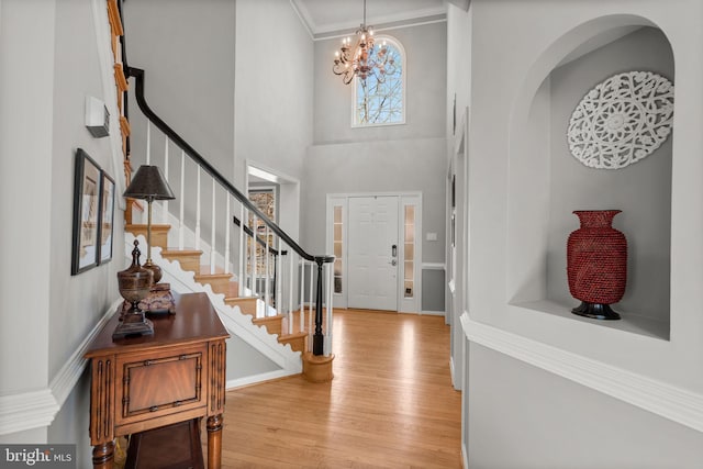 entryway featuring stairway, light wood finished floors, a high ceiling, ornamental molding, and a notable chandelier