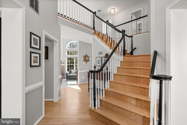 staircase featuring visible vents, baseboards, wood finished floors, and a towering ceiling