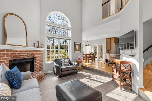 living area featuring wood finished floors, stairway, baseboards, a brick fireplace, and a chandelier