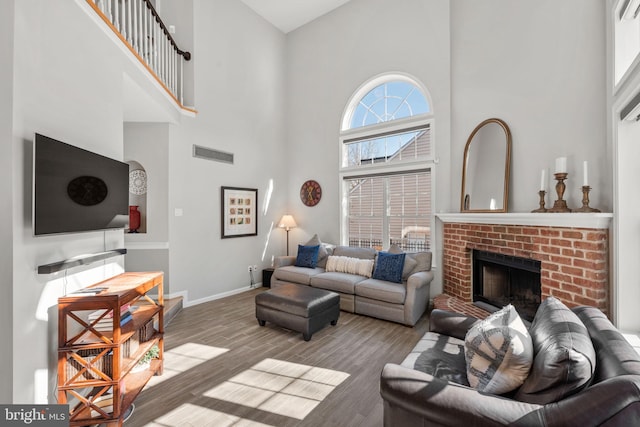 living room featuring visible vents, a brick fireplace, wood finished floors, and a towering ceiling