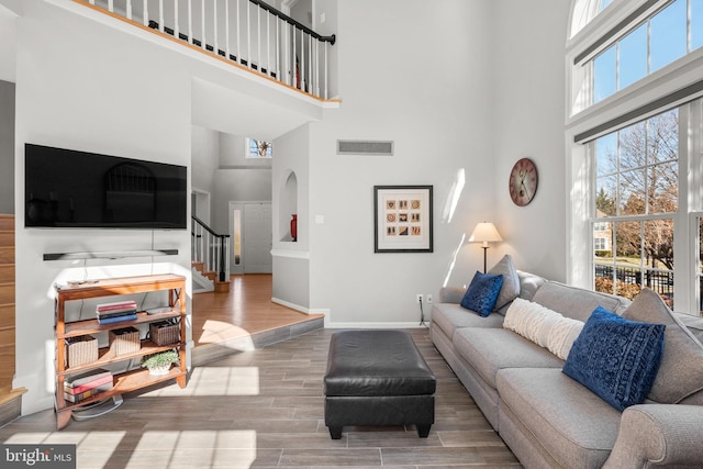 living room featuring visible vents, baseboards, wood finished floors, and a towering ceiling