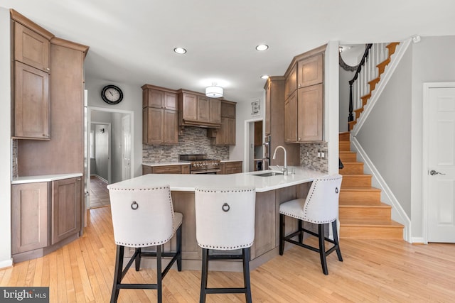 kitchen featuring a breakfast bar, high end stainless steel range, a sink, light wood-style floors, and a peninsula