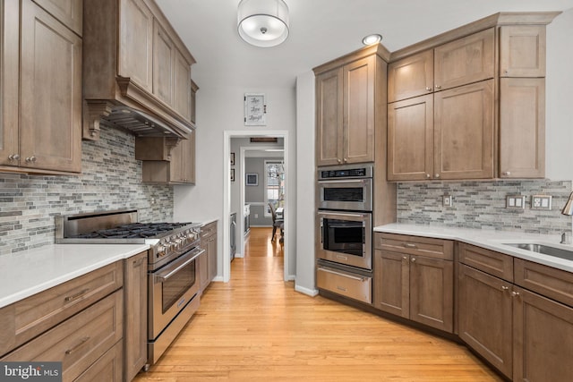 kitchen featuring light wood finished floors, tasteful backsplash, stainless steel appliances, a warming drawer, and a sink