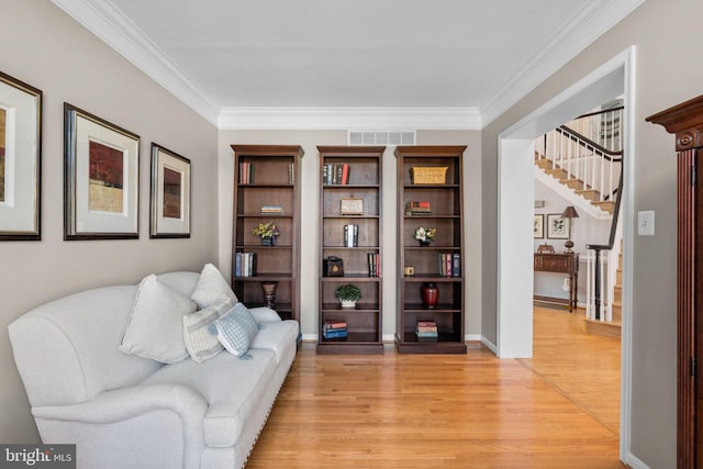 living area with stairway, visible vents, light wood finished floors, and ornamental molding