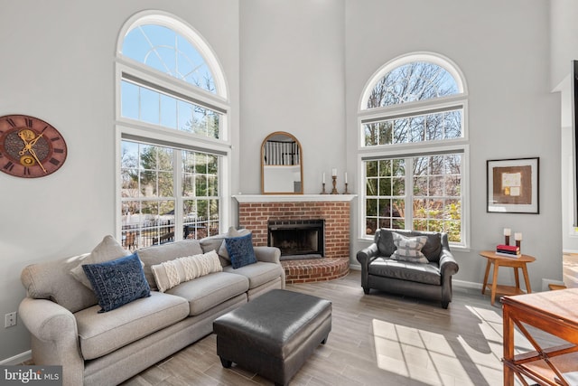 living area with a fireplace, wood finished floors, baseboards, and a towering ceiling