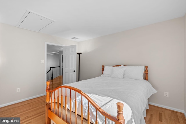 bedroom with light wood finished floors, visible vents, attic access, and baseboards