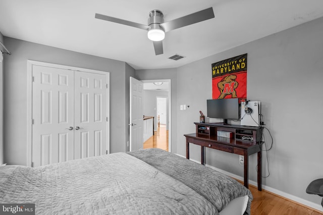 bedroom with a ceiling fan, wood finished floors, visible vents, baseboards, and a closet