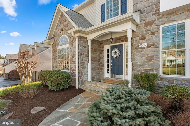 entrance to property with stone siding and roof with shingles