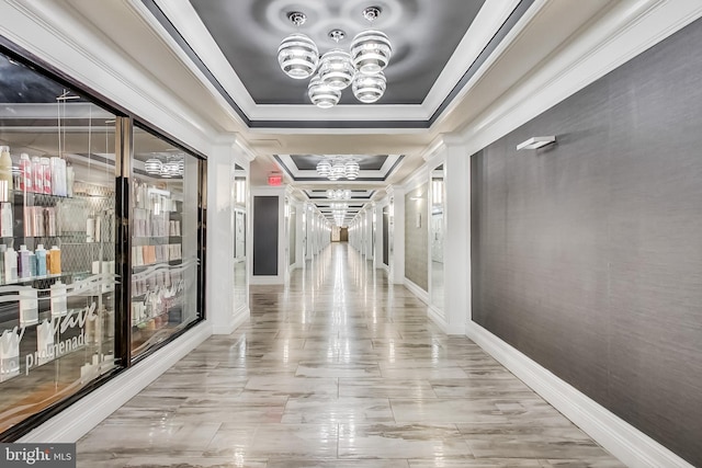 corridor featuring a chandelier, a tray ceiling, baseboards, and crown molding