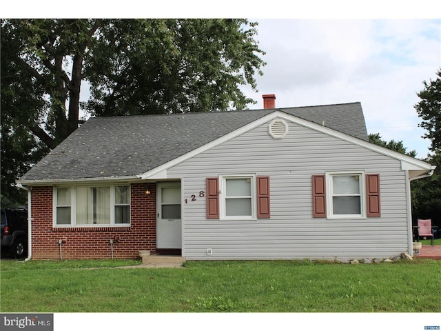 view of front of property featuring brick siding, a chimney, a front lawn, and roof with shingles