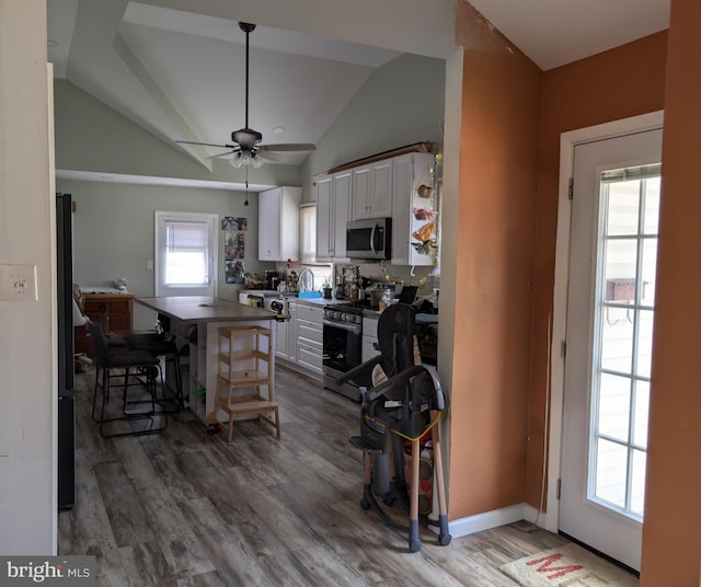 kitchen featuring a center island, vaulted ceiling, wood finished floors, white cabinets, and stainless steel appliances