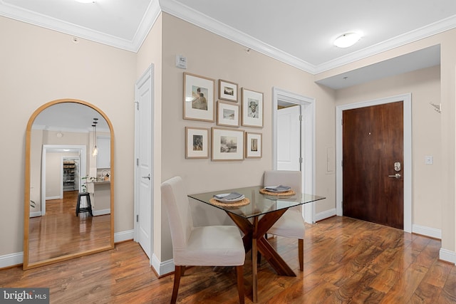 dining area featuring arched walkways, crown molding, and wood finished floors