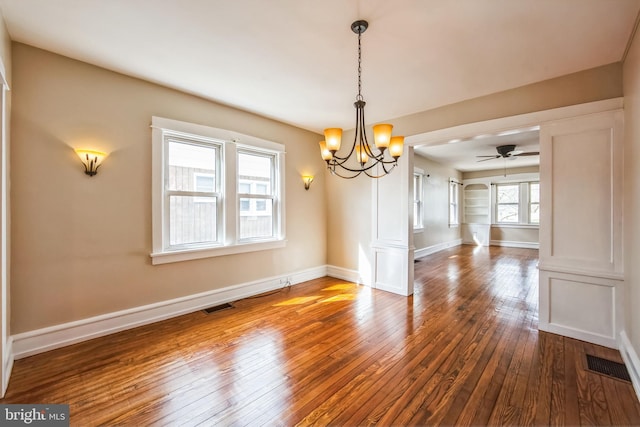 unfurnished dining area featuring dark wood-style floors, visible vents, baseboards, and ceiling fan with notable chandelier