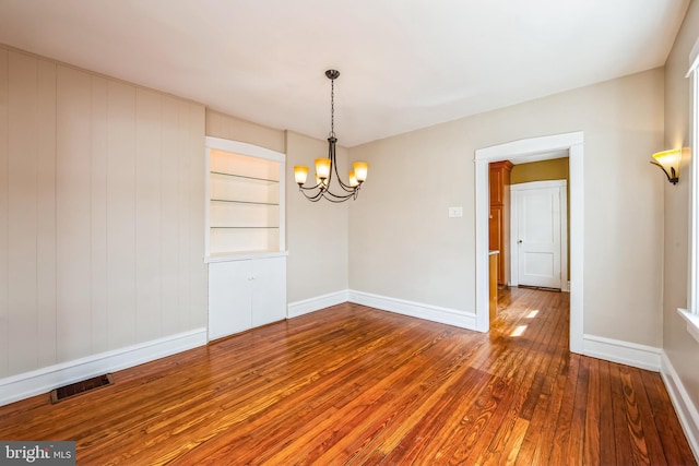 unfurnished room with built in shelves, visible vents, a chandelier, baseboards, and hardwood / wood-style flooring